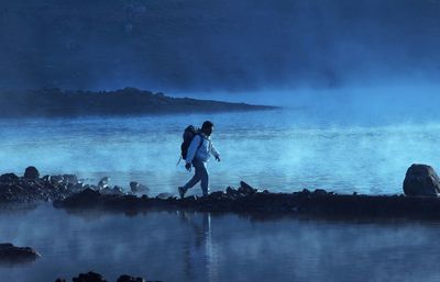 Full length of man walking at beach against cloudy sky at dusk