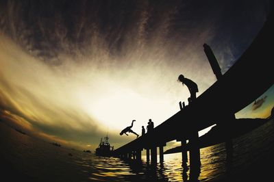Silhouette man by sea against sky during sunset