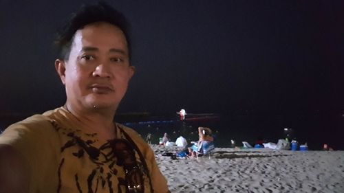 Portrait of young man on beach against sky at night