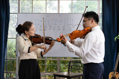 Student learning how to play violin with teacher in classroom