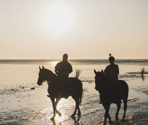Two people riding horses on beach