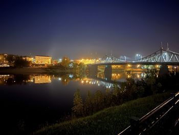 Illuminated bridge over river in city against sky at night