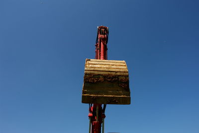 Low angle view of earth mover against clear blue sky