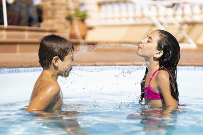 Sister spitting water on brother in swimming pool