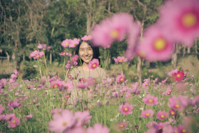Portrait of smiling young woman with pink flowers on field