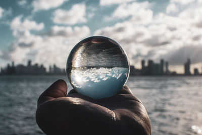 Close-up of hand holding crystal ball against water