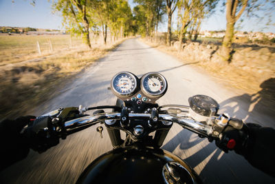 Back view of faceless fast racer riding motorbike through forest in rural location