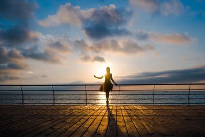 Silhouette woman by sea against sky during sunset