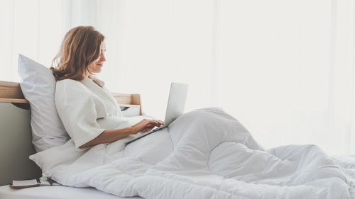 Woman using mobile phone while sitting on bed at home