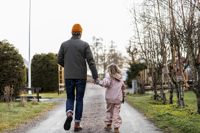 Full length rear of view father and daughter holding hands while walking on road