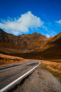 Empty road by mountains against blue sky