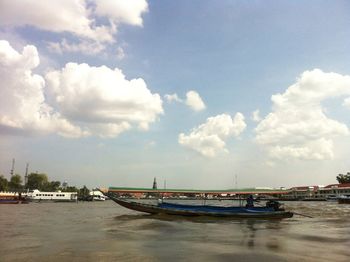 Boats in river against cloudy sky