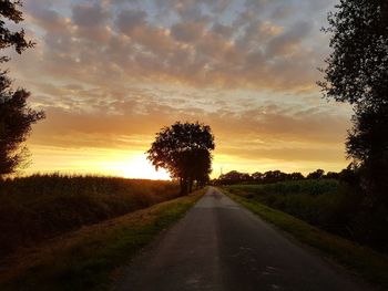 Road amidst silhouette trees against sky during sunset