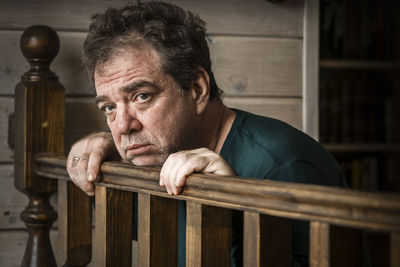 Portrait of man leaning on wooden railing at home