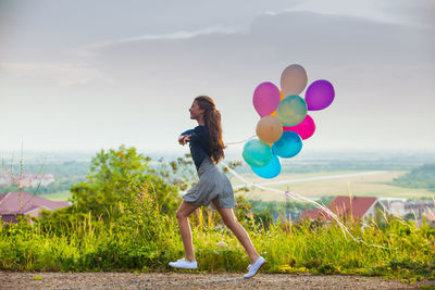 Rear view of woman with balloons standing on field against sky
