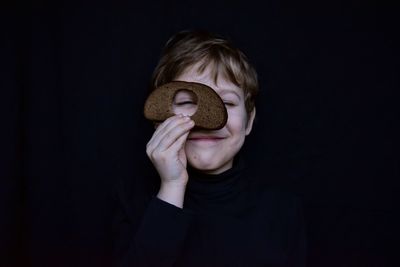Close-up of boy holding bread against black background