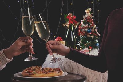 Midsection of women toasting champagne flutes against christmas decoration