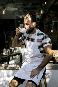 Young male owner drinking coffee while sitting outside cafe