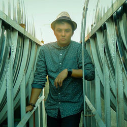 Portrait of young man wearing hat while standing amidst metallic structure