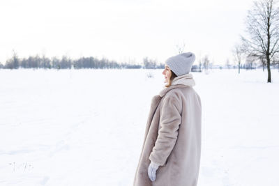 Young girl in beige clothes, fur coat made of artificial fur walks in winter