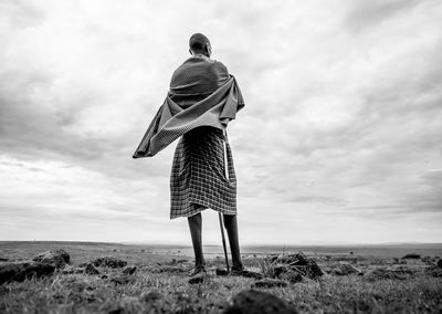 Rear view of man standing on field against cloudy sky