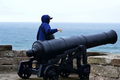 Man standing by historic cannon while looking at sea