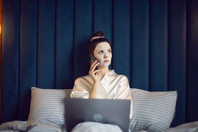 Woman applies cleansing mask on her face. female businessman a freelancer works on a laptop on bed.