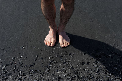 Low section of man standing at black sand beach