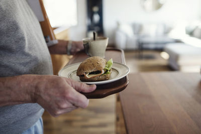 Midsection of senior man holding tray with sandwich and cup at home