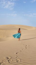 Woman with long dress on sand dune in desert against sky