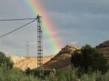 Electricity pylon by mountain against sky