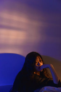 Side view of woman sitting on beach against sky during sunset