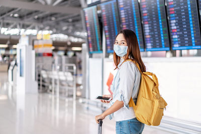 Young woman looking at camera while standing on mobile phone