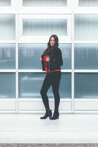 Full length portrait of young woman standing against glass wall