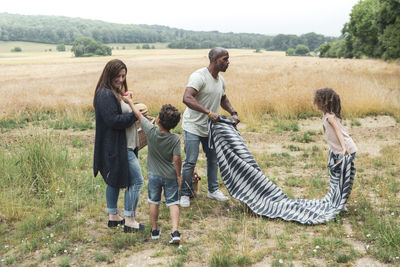 Boy giving apple to mother while father and sister placing blanket on field