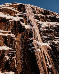 Low angle view of icicles on rock against sky