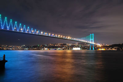 Illuminated bridge over sea against sky at night