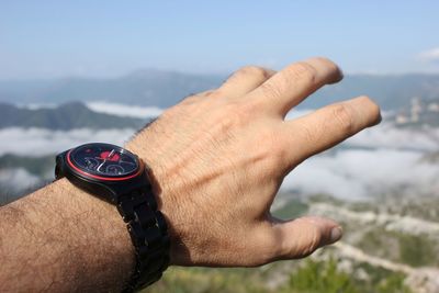 Close-up of cropped hand wearing wristwatch against sky