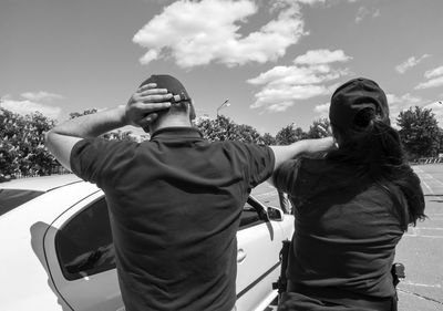 Rear view of man and woman by car against sky