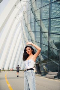 Portrait of young woman shielding eyes standing against building in city