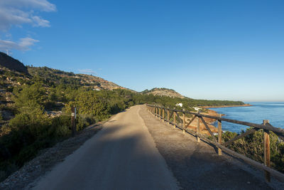 Scenic view of road by sea against blue sky