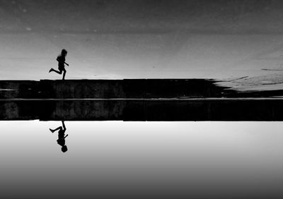 Silhouette person by swimming pool against sky