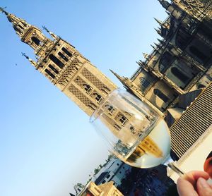 Low angle view of hand holding ice cream against sky
