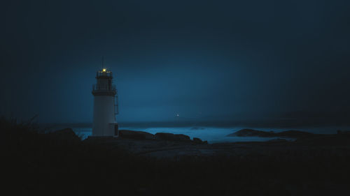 Lighthouse by sea against clear sky