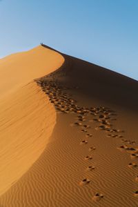 Footprints on sand dune in desert against clear sky