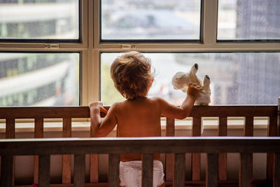 Rear view of shirtless boy looking through window