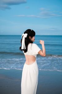 Side view of young woman standing at beach against sky