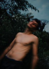 Shirtless young man standing in forest