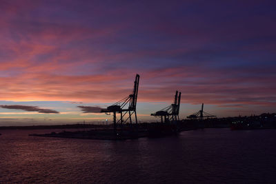 Silhouette cranes against sky during sunset