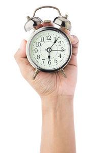 Cropped hand holding alarm clock against white background